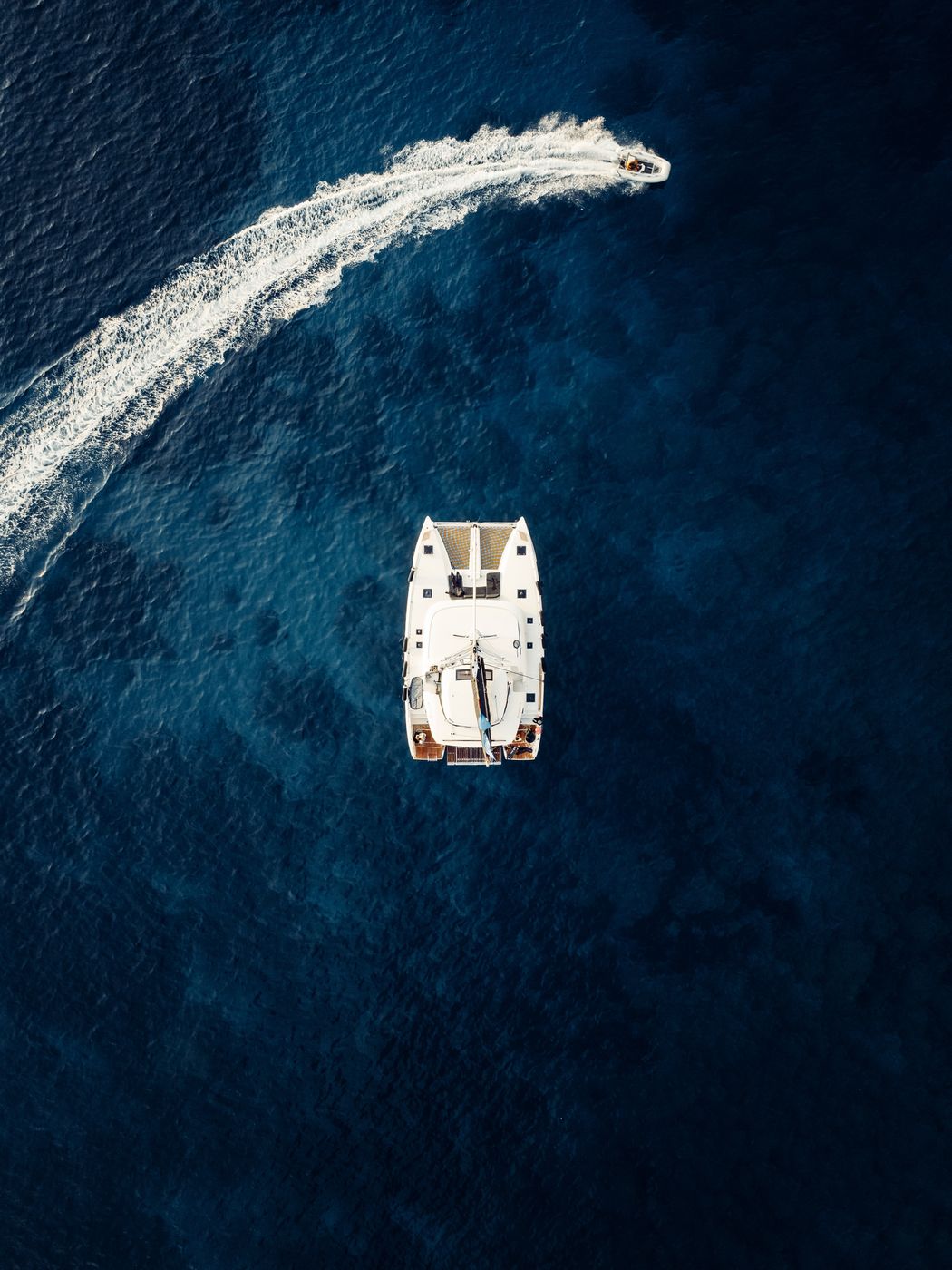 Catamaran from above on deep blue water with a white wake