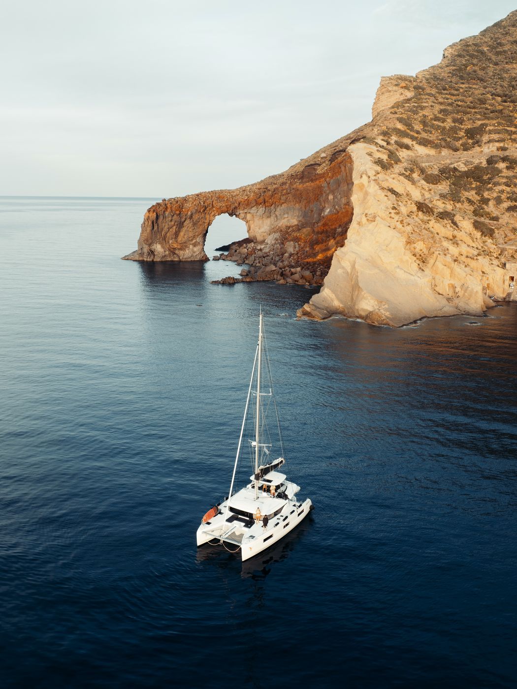 Catamaran below a rock arch at golden hour