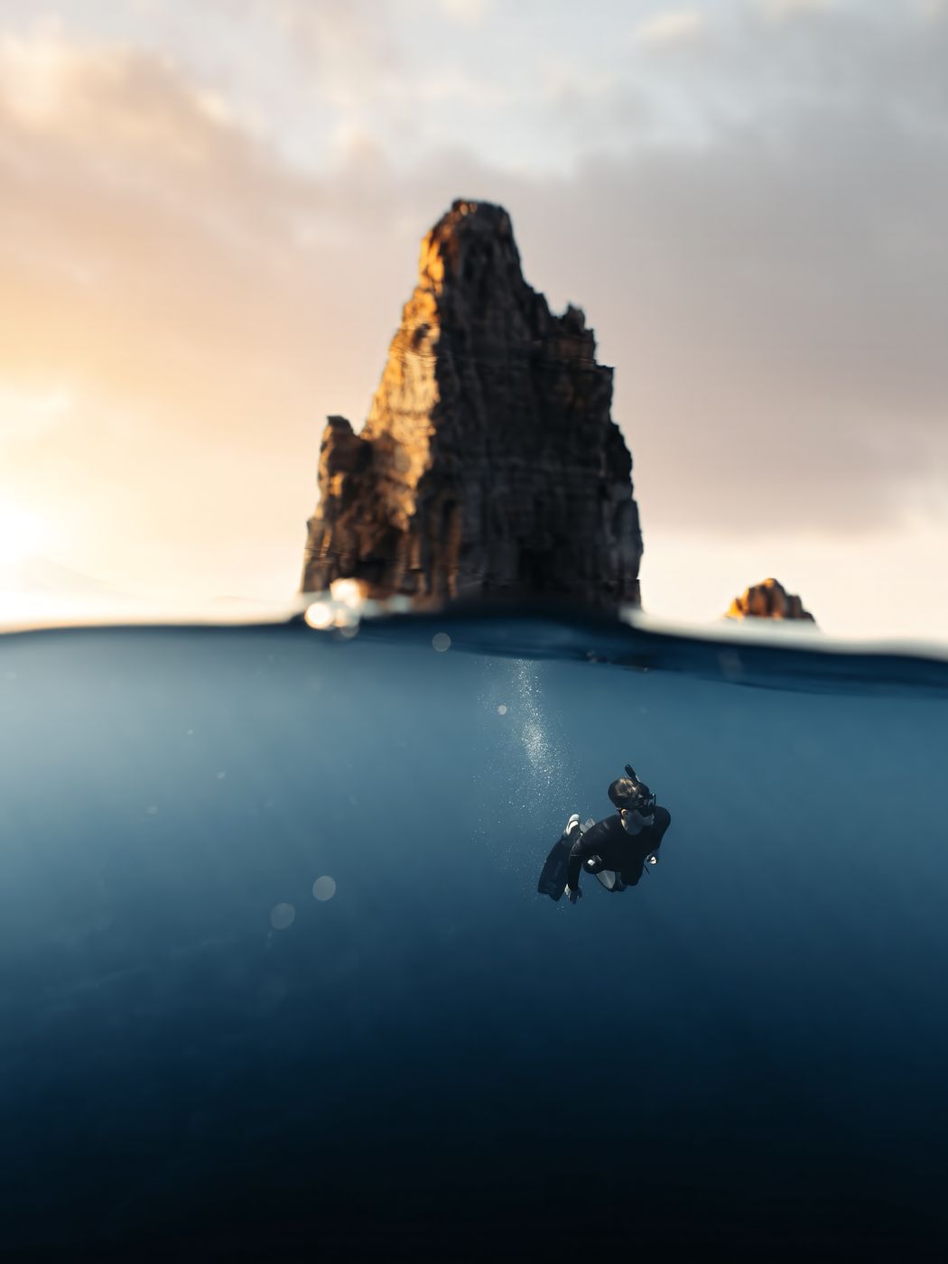 Freediver below the surface under a sea stack, half above half below water