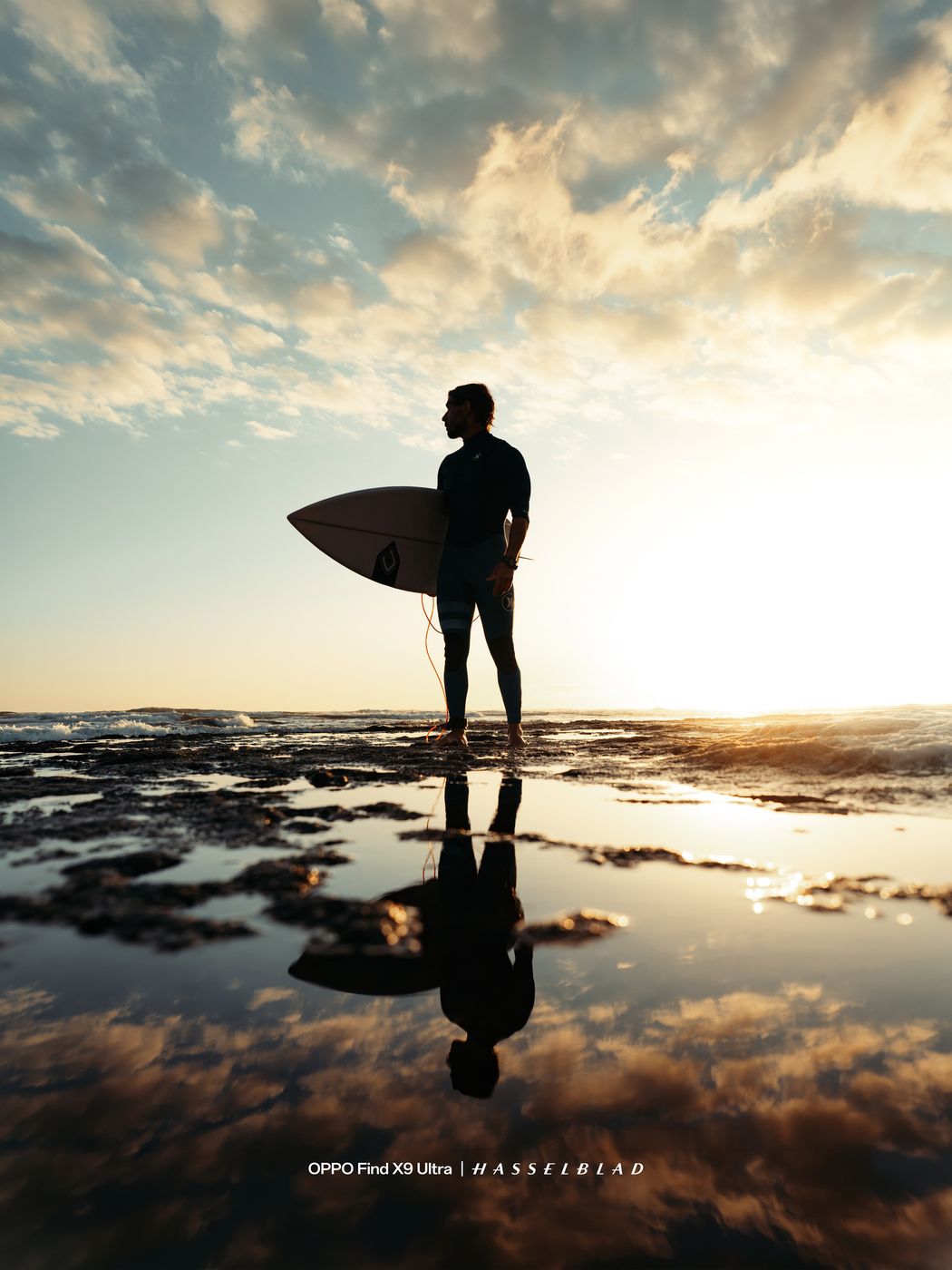 Surfer with a board reflected in tide pools at sunset