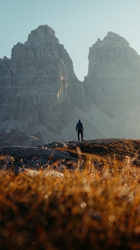 A hiker standing below the Tre Cime walls in golden grass