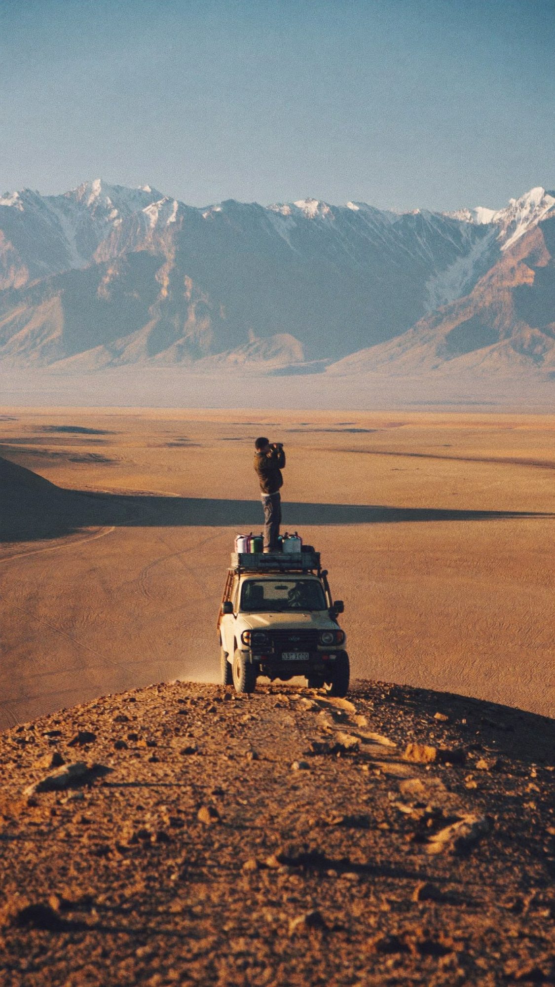 A person standing on the roof of a 4x4 on a desert ridge