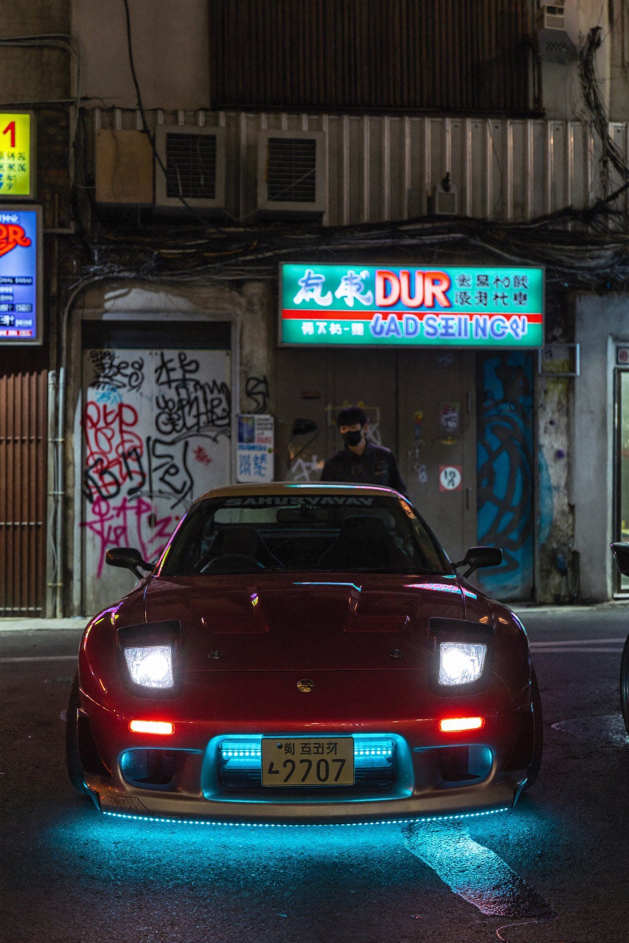 Red sports car with blue underglow in a Tokyo alley at night